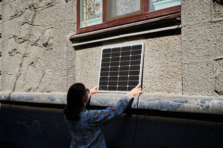 Woman holding photovoltaic solar panel in front of historical building, wearing plaid shirt and...