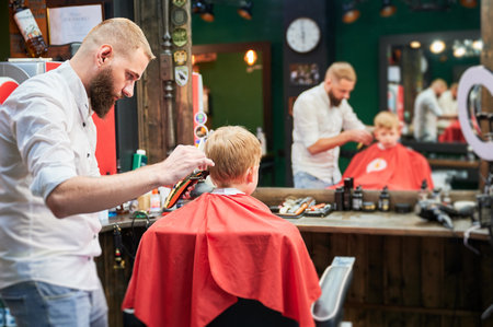 Barber using comb and shaver to cut hair. Professional hairdresser shaving little kids nape.の写真素材