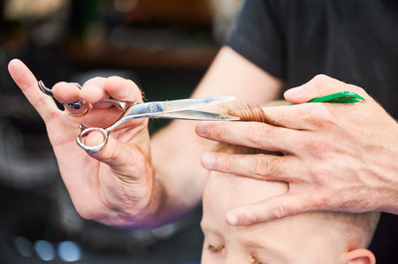 Close up view of professional barber cutting boys hair. Little blond boy getting new haircut. Cropped photo of kids hair cutting.の写真素材