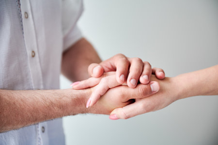 Close up of two hands engaging in delicate touch. Mans and womans hands on white neutral background. Husband holding hand of his lovely wife. Concept of love, intimacy, support, and trust.の写真素材