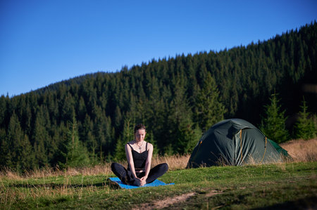 Woman practicing yoga and meditating outdoors in the mountains in a serene, natural setting. Female performing yoga pose on mat.の写真素材