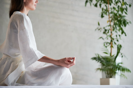 Beautiful woman in white dress sitting on mat in lotus position before Thai massage, practicing yoga.の写真素材