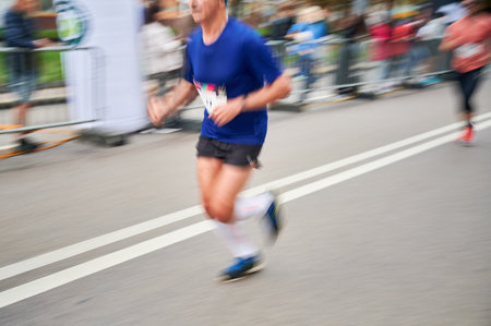 Close-up shot of runners legs in motion, showing powerful stride as race down street, with blurred spectators in background emphasizing speed and intensity of moment.の写真素材