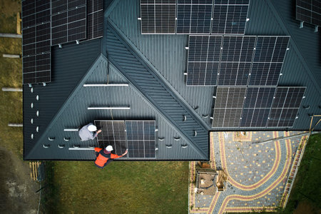 Electricians building photovoltaic solar module station on roof of house. Men technicians in helmets...