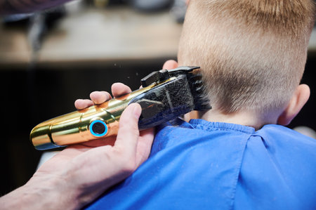 Back view of hairdresser shaving boys head. Competent barber using electric shaver. Little client getting stylish mens haircut.の写真素材