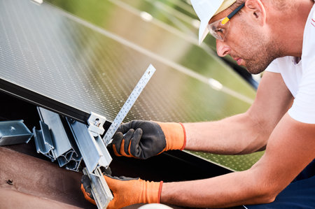 Worker building solar panel system on rooftop of house for generating electricity through photovoltaic effect. Man using ruler to measure mounting equipment for precise installation.の写真素材