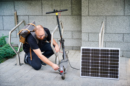 Man connects solar panel to electric scooter for charge. Integration of solar power as sustainable energy source for charging electric scooters, promoting eco-friendly urban transportation.の写真素材