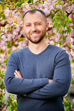 Man allergic enjoying after treatment from seasonal allergy at spring. Portrait of happy bearded man smiling in front of blossom tree at springtime. Spring allergy concept.の写真素材