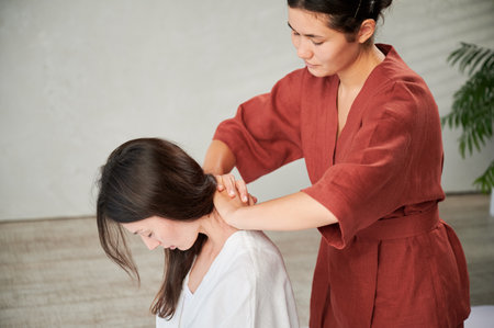 Masseuse making thai yoga massage. Woman therapist doing traditional massage treatment for female patient indoors. Client sitting, meditating, enjoying hand massage in calm atmosphere.の写真素材