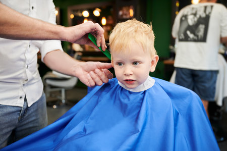 Cute boy getting stylish haircut. Hairdresser in process. Little client first time in barbershop.の写真素材