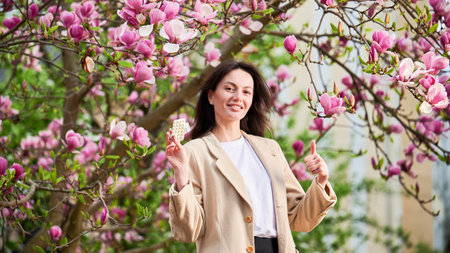 Woman allergic suffering from seasonal allergy at spring, posing in blossoming garden at springtime. Young happy woman showing holding pack of pills, giving thumbs up. Antihistamine medication conceptの写真素材