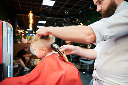 Barber using comb and shaver to cut hair. Professional hairdresser shaving little kids nape.の写真素材