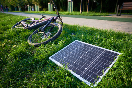 Pink electric mountain bike lies on lush green grass, connected to solar panel for charging. Bicycle beside paved path, showcasing bikes rugged tires and sleek design in outdoor environment.の写真素材