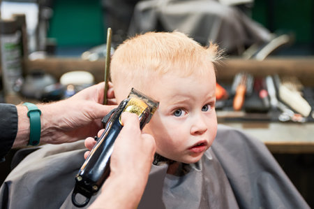 Barber using comb and shaver to cut hair. Professional hairdresser shaving little kids nape. Close up.の写真素材