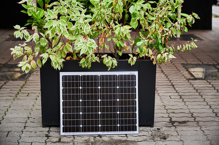 Photovoltaic solar panel at large planter filled with vibrant green foliage, set on paved area under canopy. Urban setting emphasizes integration of green energy solutions within modern cityscapes.の写真素材