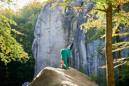 Woman practicing yoga outdoors in forest. Barefoot female on yoga mat surrounded by trees and large rocks, which suggests peaceful, natural environment ideal for meditation or yoga practice.の写真素材