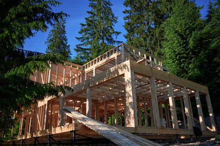 Residential building with wooden frame in process of being built near a forest. Beginning of new construction of comfortable cottage. Idea of ecological construction, contemporary architectural designの写真素材