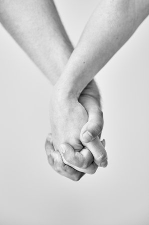 Two hands held together in grasp against neutral background. Close up of mans and womans hand. Concept of intimacy, support, and trust. Black and white image.の写真素材