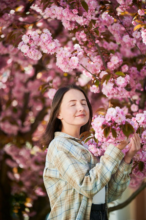 Woman allergic enjoying after treatment from seasonal allergy. Portrait of happy beautiful woman smiling with eyes closed in front of blooming sakura tree at springtime. Spring allergy concept.の写真素材