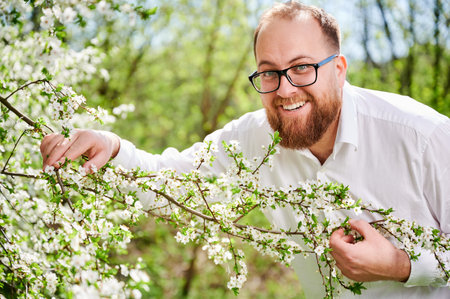 Man allergic enjoying after treatment from seasonal allergy at spring. Portrait of happy bearded man smiling in front of blossom tree at springtime. Spring allergy concept.の写真素材