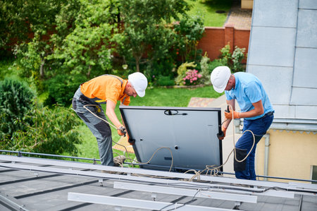 Men workers installing solar panel system on roof of house. Electricians in helmets lifting up photovoltaic solar module with help of ropes outdoors. Concept of alternative and renewable energy.の写真素材