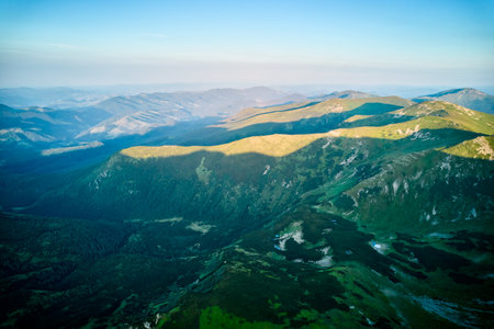 Aerial view of rugged mountain range with lush green slopes at sunset. Landscape showcases beauty of untouched nature with distant peaks and valleys bathed in soft sunlight. Carpathians, Chornogora.の写真素材