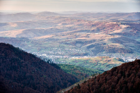 Panoramic photo mountain valley bathed in soft, golden light. Small town nestled in valley, surrounded by rolling hills and fields. Distant mountains fade into horizon, creating sense of depth.の写真素材