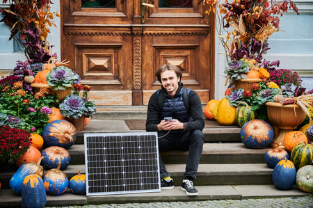 Man using smartphone connected to photovoltaic solar panel. Integration of sustainable renewable energy into everyday life, demonstrating practical use of solar power for charging devices.の写真素材