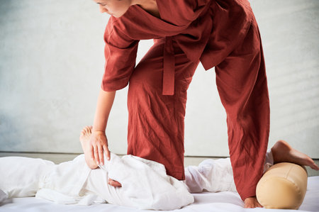 Masseuse making thai yoga massage. Woman therapist doing traditional massage treatment, stretching female patients body. Client lying on mat, enjoying hand massage in calm atmosphere. Cropped view.の写真素材