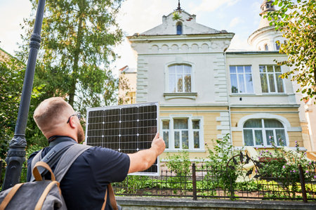 Man holding photovoltaic solar panel in front of historical building. Concept of integration of sustainable renewable energy sources into architecture.の写真素材