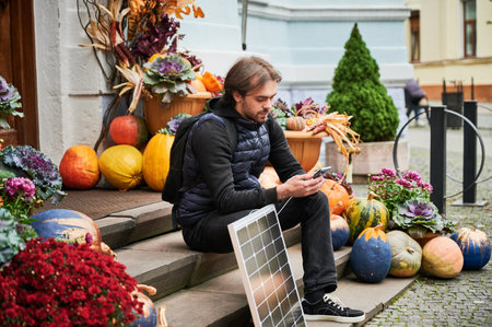 Handsome man using smartphone connected to photovoltaic solar panel. Integration of sustainable renewable energy into everyday life, demonstrating practical use of solar power for charging devices.の写真素材