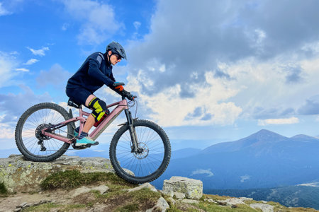 Cyclist man riding electric mountain bike outdoors. Male tourist biking along grassy trail in the mountains, wearing helmet. Concept of sport, active leisure and nature.の写真素材