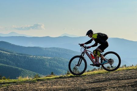 Cyclist man riding electric mountain bike outdoors. Male tourist biking along grassy trail in the mountains, wearing helmet and backpack. Concept of sport, active leisure and nature.の写真素材