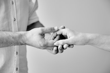 Close up of two hands engaging in delicate touch. Mans and womans hands on white neutral background. Husband holding hand of his lovely wife. Concept of support, mutual respect. Black and white.の写真素材