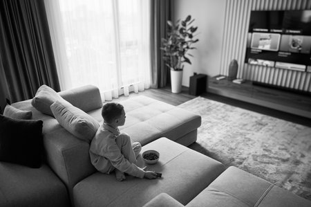 Lazy morning for little boy. Cute kid eating cereals and watching favorite TV show. Joyful child...