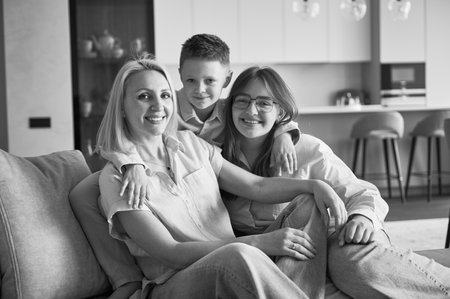 Lovely family relaxing on couch in living room. Little boy hugging his sister and mom. Cozy spending...