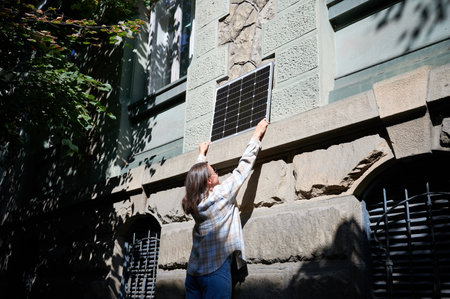 Woman holding photovoltaic solar panel in front of historical building, wearing plaid shirt and...