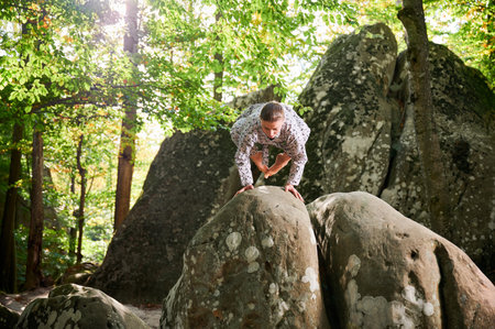 Woman practicing yoga outdoors in forest. Barefoot female on yoga mat surrounded by trees and large rocks, which suggests peaceful, natural environment ideal for meditation or yoga practice.の写真素材