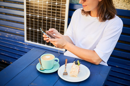 Young woman charging her smartphone from solar panel while relaxing. Pretty girl drinking coffee and checking her phone next to solar battery. Conscious female choosing sustainable lifestyle.の写真素材