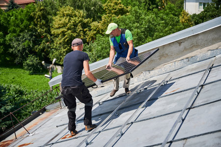 Workers building solar panel system on metal rooftop of house. Two men installers carrying photovoltaic solar module outdoors. Alternative, green and renewable energy generation concept.の写真素材