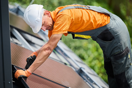 Worker building photovoltaic solar panel system on rooftop of house. Man engineer in helmets and gloves installing solar module with help of hex key outdoors. Renewable energy generation concept.の写真素材