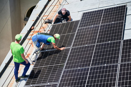 Workers building solar panel system on metal rooftop of house. Three men installers installing photovoltaic solar module outdoors. Alternative, green and renewable energy generation concept.の写真素材