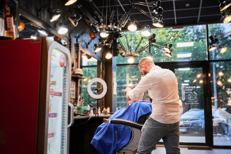 Man barber cutting little boys hair using comb and scissors. Child getting haircut from adult male, likely barber. Professional hairdresser and cute client at modern barbershop.の写真素材