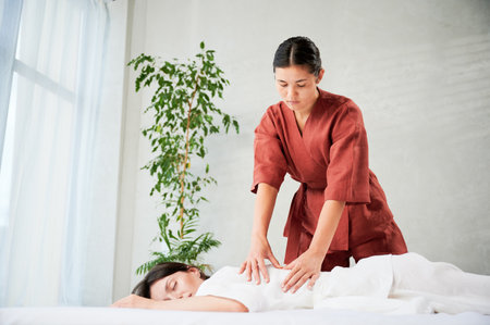 Masseuse making thai yoga massage. Woman therapist doing traditional massage treatment for female patient indoors. Client lying on mat, meditating, enjoying hand massage in calm atmosphere.の写真素材