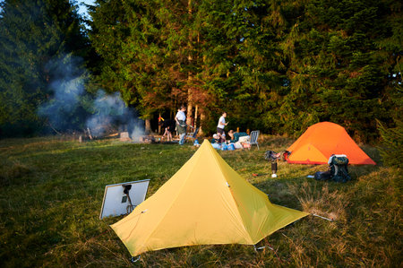 Solar panel in grassy field with tents in background highlights eco-friendly camping setup. Scene includes campers, emphasizing integration of renewable energy in outdoor activities.の写真素材