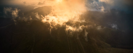 Stunning aerial view of mountain landscape at sunrise, with suns golden rays piercing through mist and clouds, casting magical glow over peaks, creating serene and ethereal atmosphere. Aerial view.の写真素材