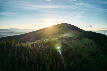 Aerial view of serene mountain landscape at sunset. Forested hills bathed in warm, golden light, creating tranquil atmosphere. Rolling hills stretch into the distance, covered in dense, lush greenery.の写真素材