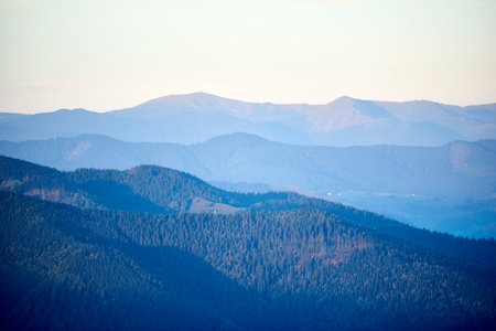 Serene view of rolling mountains in shades of blue and green, with distant peaks under soft, pastel sky, creating peaceful and tranquil landscape.の写真素材