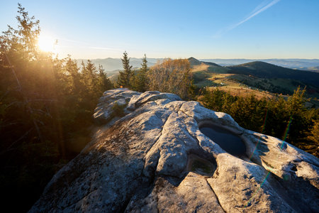 Scenic sunrise at Pysanyi Kamin in Carpathians, Ukraine. Rocky surface in foreground. Breathtaking view of rolling hills, dense forests, and distant mountains illuminated by soft morning light.の写真素材