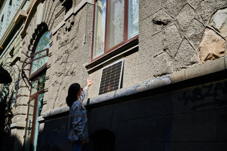 Woman holding photovoltaic solar panel in front of historical building, showing Ok sign. Concept of integration of sustainable renewable energy sources into old architecture.の写真素材